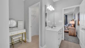 whipering-winds-slider-images 6 | Swack Vacations Hallway bathroom with white cabinets and marble countertop, large mirror, and bright light fixtures; doorway opens to a bedroom with a nightstand and bed.