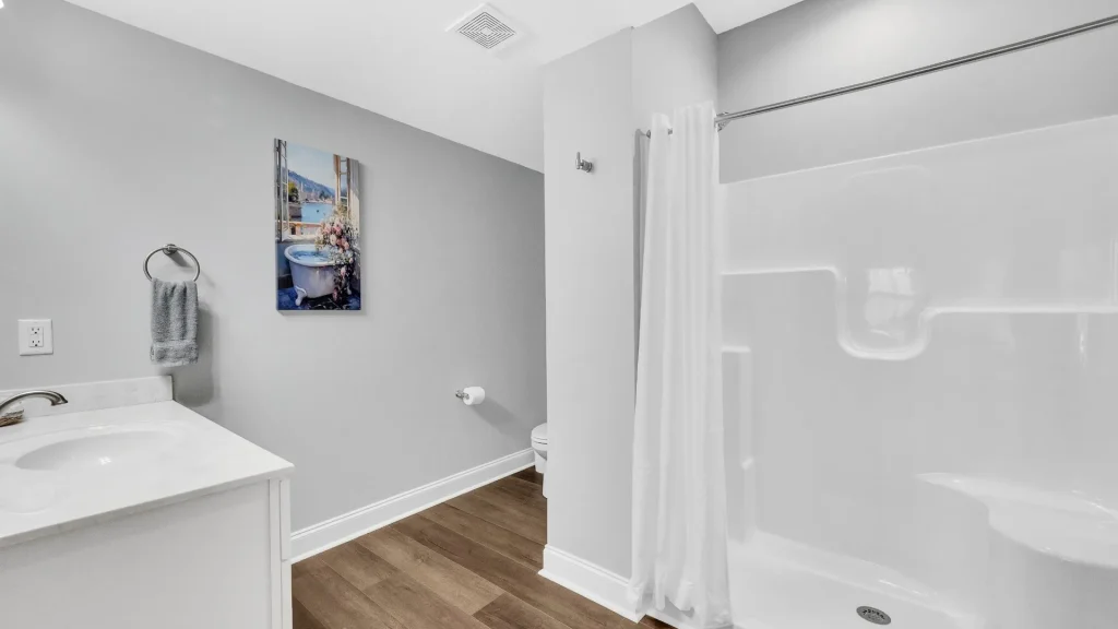 Modern bathroom with white vanity, towel ring, and a wall-mounted painting beside a gray wall.