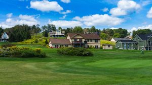 Houses on a manicured golf course with green fairways and a bright blue sky with white clouds in the background.