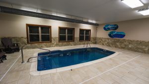 Indoor pool area with beige tile, metal handrails, and a stone wainscoting wall; windows overlook darkness outside; themed skate murals say 'Beary Fine Resort' on the right.