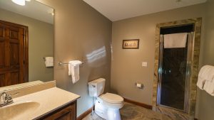 Bathroom with beige walls, vanity mirror, and granite countertop; toilet and towel bars visible by a glass shower enclosure.
