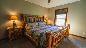 Rustic log-bedroom with a heavy wooden bed, matching nightstands, and warm lamps on each side.