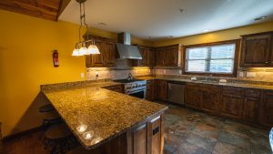 Bright yellow kitchen with dark wood cabinets, granite countertops, and a central island with bar stools under a hanging light fixture.