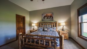 Rustic log bed in a light-green bedroom with matching nightstands, bear-themed bedding, and a bear wall art above the headboard.