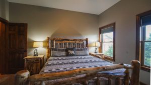 Rustic bedroom with a log bed, matching nightstands, and a bear-pattern quilt; soft lamps illuminate the wood tones.