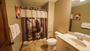 Bathroom with a bear-themed shower curtain, wall art of a bear, and white towels on a beige wall (informational image).