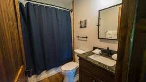 Small bathroom with a dark blue shower curtain, white toilet, and a black granite countertop with a sink. Wooden trim frames the space.