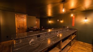 Warm, dimly lit bar interior with marble counter, wooden doors, and hanging cage lights; beer sign on wall in the background
