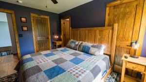 Bedroom with dark blue walls and a large wooden bed, patchwork quilt, and matching nightstand lamp.