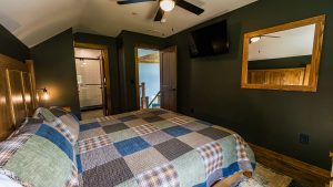 Cozy bedroom with dark green walls, a plaid quilt on a wooden bed, and a ceiling fan above.