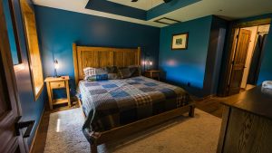 Blue-walled bedroom with a large wooden bed, plaid quilt, and two matching nightstands with lamps on each side.