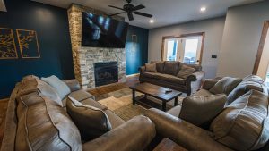 Cozy living room with a stone fireplace, mounted TV, and a ceiling fan, surrounded by gray sectional sofas and a wooden coffee table.