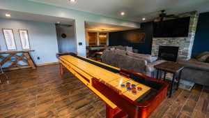 Pool-table-forward view in a spacious game room with a leather sofa, stone fireplace and a large wall-mounted TV in the background.