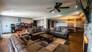 Spacious basement recreation room with arcade games, a pool table, and a large gray sectional sofa arrangement.