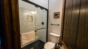Modern bathroom with a glass shower enclosure, white subway tiles, and dark fixtures, plus wood-paneled walls and a beige towel racked on the glass door.