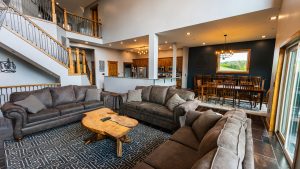 Open living area with gray sectional sofas around a live-edge wood coffee table, staircase, and kitchen-dining backdrop.