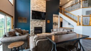 Cozy living room with a stone fireplace, wall-mounted TV, dark blue accent wall, and a wooden staircase railing.