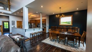 Open-concept kitchen and dining area with wood cabinets, stainless appliances, and a long wooden table with bar stools at the island.