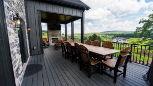 Outdoor covered deck with a long wooden dining table and Adirondack chairs, overlooking a green valley.**