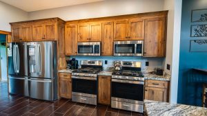 Modern kitchen with tall wooden cabinets and stainless steel fridge, microwave, and double ovens above a granite counter.