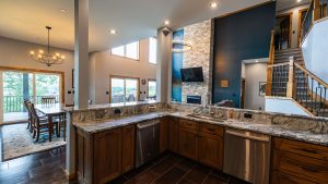 Open-concept kitchen with a granite island, wooden cabinets, and a stone fireplace visible in the living area.
