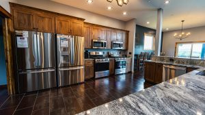 Modern kitchen with stainless steel refrigerator, double ovens, microwave, dark wood cabinets, and a granite island.