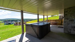 Covered patio with a hot tub under a metal roof, looking out over a grassy yard and distant houses.