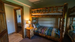Rustic log bunk bed bedroom with a lamp on a wooden nightstand and green walls in a cozy cabin-style room.