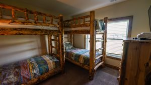 Rustic log bunk beds with patchwork quilts in a sunlit cabin-style bedroom.