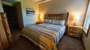 Rustic log bed with quilted blue-green bedding and two matching pillows in a cozy cabin-style bedroom.