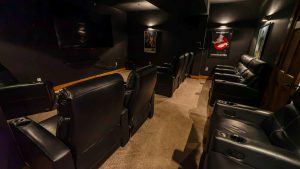 Dimly lit home theater with two rows of black leather recliners and wall movie posters in a dark room.