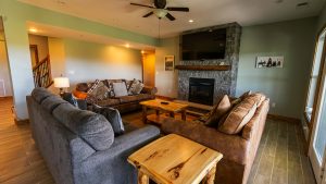 Cozy living room with a gray sectional, wooden coffee table, and a stone fireplace with a mounted TV above it.
