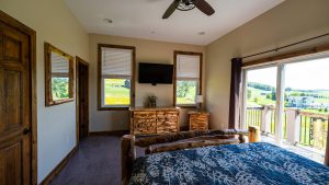 Rustic bedroom with log furniture, large windows, and a sliding glass door opening to a green landscape outside.