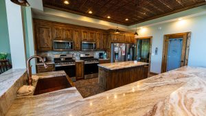 Rustic kitchen with dark wood cabinets, stainless steel fridge/ovens, marble countertops, and a central island.