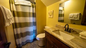 Bathroom with yellow walls, striped shower curtain, white towels, and marble countertop with a dark faucet and mirror above.