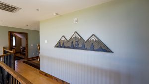 Interior staircase hall with wooden railing on left and a mountain-shaped art piece on the wall to the right, doorway visible in background.