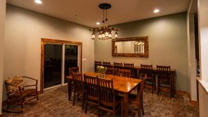 Dining room with a long wooden table, many chairs, and a rustic chandelier hanging overhead.