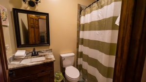 Small bathroom with a marble-topped vanity, sink and black faucet, framed mirror, and white toilet beside a striped green-and-white shower curtain.