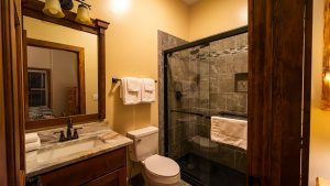 Bathroom with dark wood-framed mirrors, double vanity, towels, and a glass-enclosed gray tile shower.