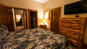 Rustic bedroom with log furniture, a patterned bedspread, and a flat-screen TV mounted above a log dresser.
