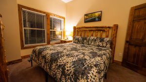 Rustic bedroom with a log-frame bed, quilted bedding, a nightstand lamp, and a landscape photo on the wall.