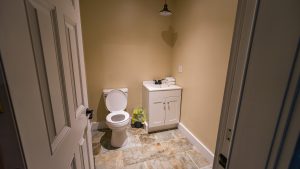 Small beige bathroom with a white toilet and a white vanity, folded towels on the counter, and a tiled floor seen from the doorway.