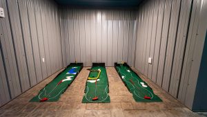 Indoor miniature golf/putting green with three lanes in a metal-walled room, flags and obstacles visible on the greens.