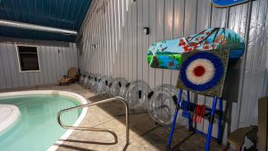 Indoor pool area with a curved pool edge, a row of clear inflatable tubes along a metal wall, and a colorful mural board nearby.