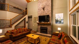 Cozy living room with a stone fireplace and mounted TV, flanked by a wooden staircase and railing.