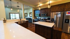 Open-concept kitchen with white marble island, dark wood cabinets, stainless steel fridge and range, pendant lighting above the island.