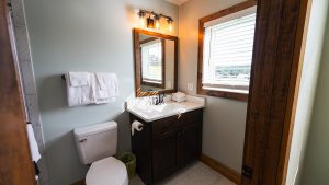 Compact bathroom with dark wood vanity, white sink, and framed mirror under a three-bulb Edison light fixture