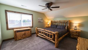Rustic bedroom with a log bed, blue patterned bedding, two wooden nightstands, and warm lamps.