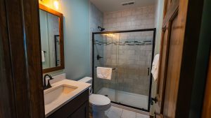 Compact bathroom with glass shower enclosure, marble tile walls, and a dark vanity with white sink and faucet.