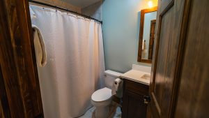 Small bathroom with a white shower curtain, toilet, and wooden vanity seen from doorway.